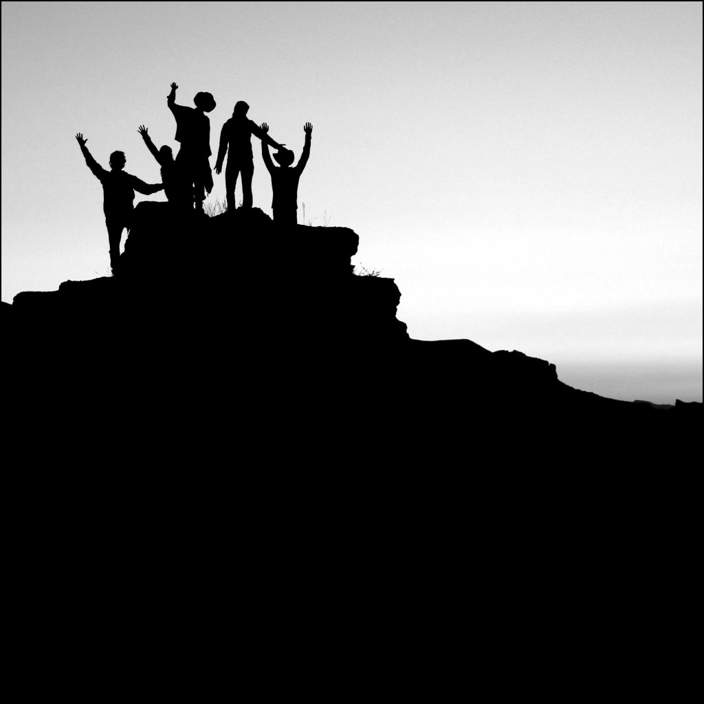 Silhouette of people cheering on a rock formation